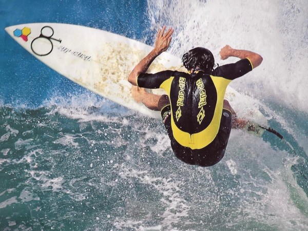 Surfer in a yellow and black wetsuit riding a wave on a surfboard.
