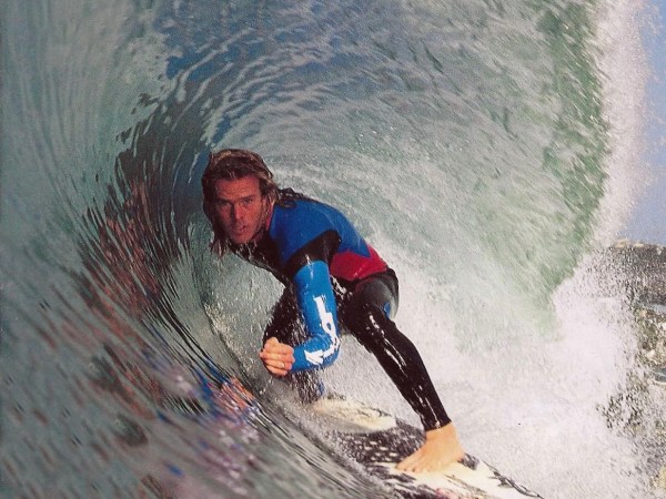 Surfer riding inside a large wave tube, wearing a blue and black wetsuit.