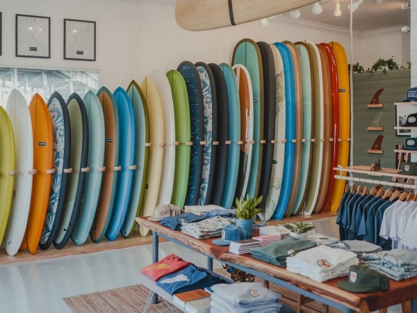 Surf shop with colorful surfboards on racks, clothing, and accessories displayed on tables and shelves.